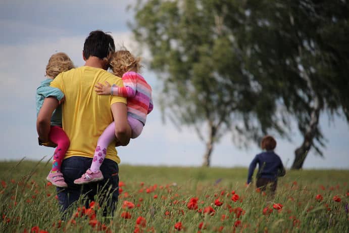 Father carrying two kids with one running away