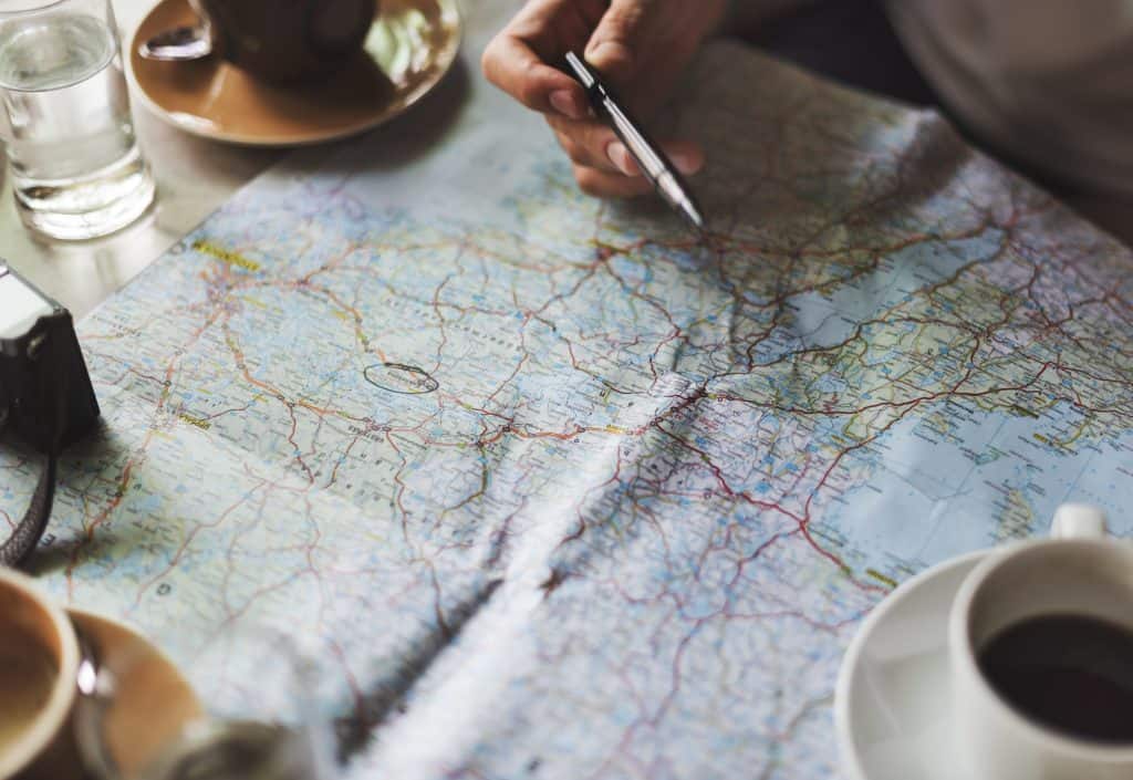 Photo of Map with beverages around it and a pen on a hand
